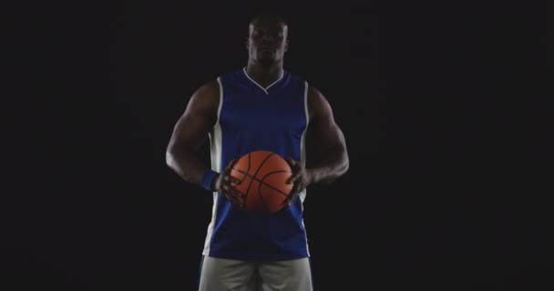 彼の前で2つの手でバスケットボールを保持し カメラを探してチームカラーを身に着けている筋肉アフリカ系アメリカ人男性バスケットボール選手の肖像画 スローモーション — ストック動画