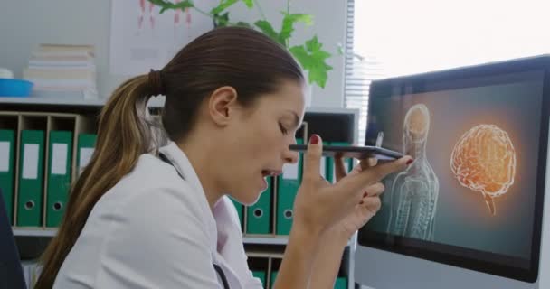 病院のオフィスの机に座ってスマートフォンで話している白人女性医療従事者の側のビュー — ストック動画