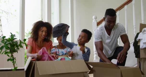 アフリカ系アメリカ人の家族と彼らの幼い息子と娘が新しい家の廊下で一緒に箱を開け カメラに笑顔 スローモーション — ストック動画