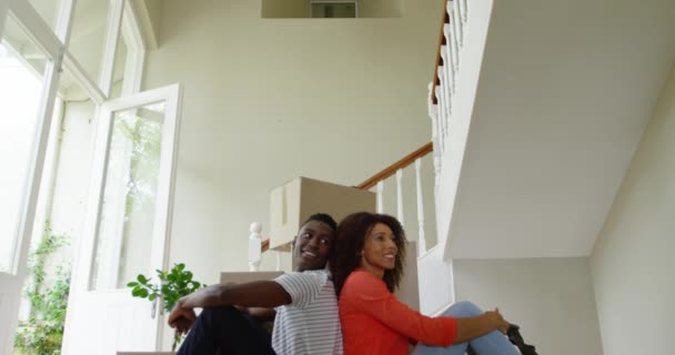 彼らの新しい家の廊下に箱の山の前に座っているアフリカ系アメリカ人のカップルの正面図は しばらくの間 移動中に休息し 周りを見回し スローモーション — ストック動画