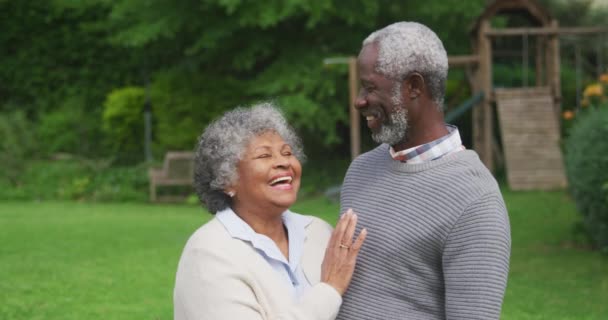 庭に身を包み 笑顔でカメラに微笑み スローモーションで立ち上がるアフリカ系アメリカ人の老夫婦の姿 — ストック動画