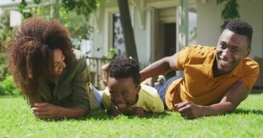 Afrika kökenli Amerikalı bir çiftin portresi. Bahçede küçük oğulları var. Güneşin altında çimlere uzanmış, kameraya gülümsüyor.