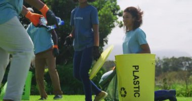 Afrika kökenli farklı bir grup yetişkin ve çocuğun tarlada eldiven ve tişört giyip üzerine gönüllü yazılar yazarak çöp ve geri dönüşüm, yavaş çekim gibi şeyler toplamalarının düşük açılı yan görüntüsü.