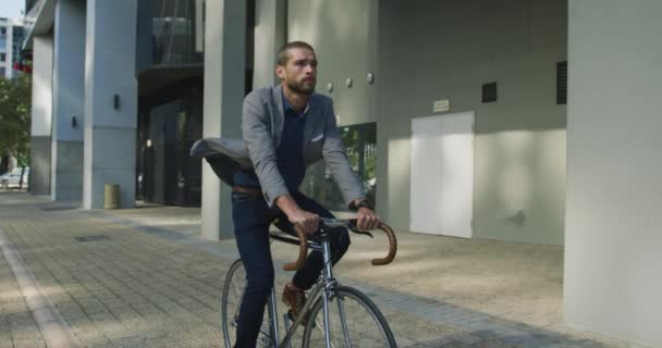 街の外出先で若い白人ビジネスマンのフロントビュー 路上で自転車に乗って スローモーション — ストック動画