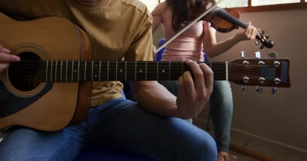 白人の十代の男性と女性のミュージシャンのリハーサルのフロントビュー 少女はバイオリンを演奏し 少年はアコースティックギターを演奏し スローモーション — ストック動画
