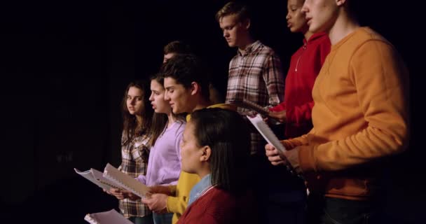多个族裔的少男少女组成的合唱团 手握乐谱 唱着歌 站在学校剧场的舞台上排练表演 动作缓慢 — 图库视频影像