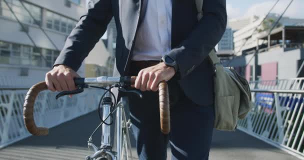 街を歩く若い白人ビジネスマンのフロントビューの真ん中のセクションでは 背景に建物と路上で自転車で歩く スローモーション — ストック動画