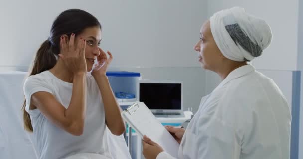 病院での診察中に白人女性患者と話をして診察する混合人種の女性医師の側の見解 — ストック動画