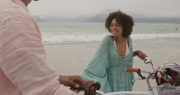 海沿いのビーチでアフリカ系アメリカ人のカップルの側のビュー 自転車を保持し 話して スローモーション ロマンチックな休暇のコンセプト — ストック動画