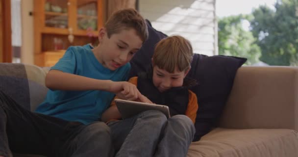 两个白人兄弟坐在客厅里 坐在沙发上 一起使用平板电脑 弟弟拿着电脑 微笑着 而哥哥则用触摸屏 慢动作4K — 图库视频影像