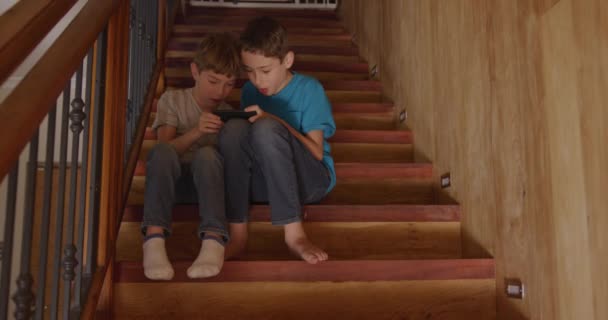 家で2人の若い白人兄弟のフロントビュー 一緒にスマートフォンを使用して階段に座って 話して笑って スローモーション4K — ストック動画
