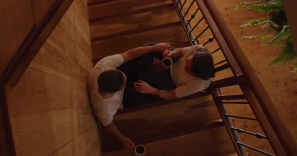 俯瞰着一对白人夫妇在家里 一起坐在楼梯上 手里拿着咖啡 慢吞吞地聊天的情景 — 图库视频影像