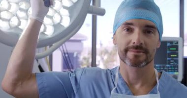 Kafkas cerrahı erkek bir cerrahın portresi. Ameliyathanede ameliyat maskesini takmış, eldiven takmış, ameliyat masasında bir lambayı tutuyor ve kameraya gülümsüyor.