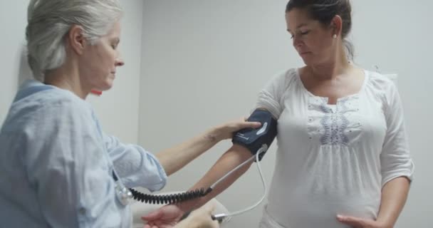 病院の白人女性医療専門家の側の見解では 妊婦の白人女性と話しながら 出生前の検査中の血圧を測定します — ストック動画