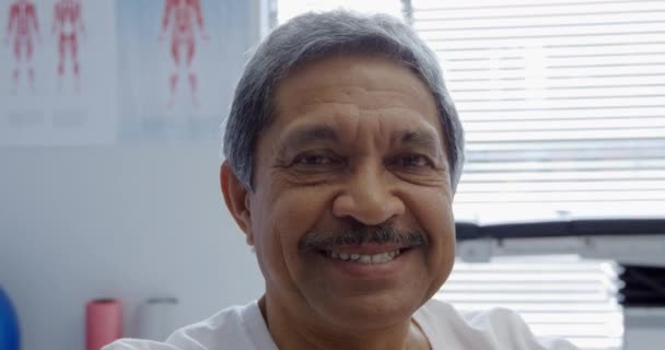在一家医院的诊疗室里 一位高年级的男女混血男子的近照出现在镜头前 面带微笑 — 图库视频影像