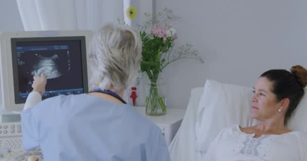 一个在医院工作的白人女性保健专业人员的后视镜 与一位高傲的白人妇女坐在病床上 同时给她做了超声波扫描 — 图库视频影像