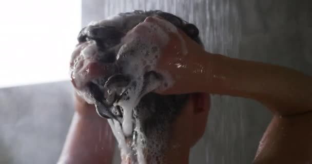 在现代化的浴室里 一个有着一头长长的黑头发的年轻白人女人站在淋浴下 洗头和洗头 动作缓慢 她的后视镜照在她的后脑勺 — 图库视频影像