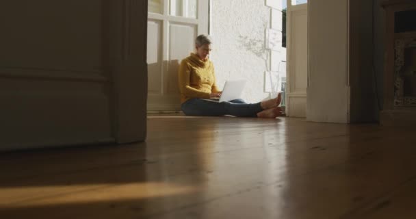 一位白种人老妇人的侧视图 她在家里留着灰白的短发 坐在前门的走廊里 用笔记本电脑 动作缓慢 — 图库视频影像