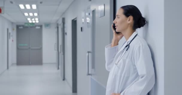 病院の廊下に研究室のコートと聴診器を身に着けている幸せな白人女性医師の側面図 スマートフォンで話して笑顔 — ストック動画