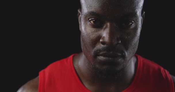 一个非洲裔美国男子运动员在训练后汗流浃背 凝视着镜头 慢镜头 黑色背景的特写 — 图库视频影像