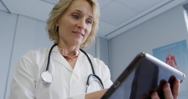 研究室のコートを着た白人女性医師のフロントビューと 病院の治療室でタブレットコンピュータを使用した聴診器 スローモーション — ストック動画