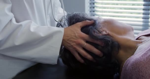 一位身穿实验室外套的白人女医生在一家医院的理疗过程中把头抬起来移动了一下 一位混血的女病人躺在沙发上 侧视近景 — 图库视频影像