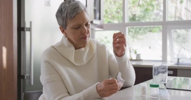 薬を見て彼女の台所で彼女の薬を見て 毎週の薬箱と彼女の横にあるカウンターの上の水のガラス スローモーション — ストック動画