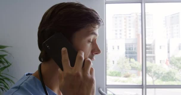 一名白人男性医务工作者站在医院的侧视图 戴着刷子站在楼梯上 用智能手机交谈 — 图库视频影像