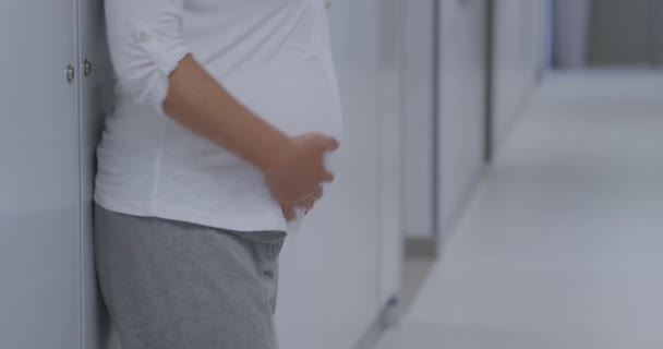 側ビューアップ妊娠中の白人女性の近くに病院の廊下に立って 彼女の腹をマッサージし 下を見ます — ストック動画