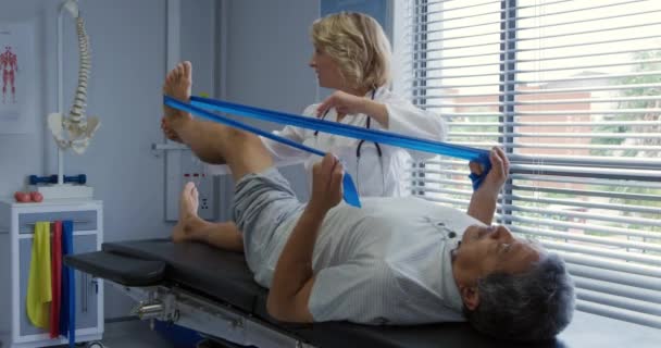 一位身穿实验室外套的白人女医生在一次理疗过程中帮助一位身披实验室外套的老年男女病人在沙发上躺着抵抗带的侧视图 — 图库视频影像