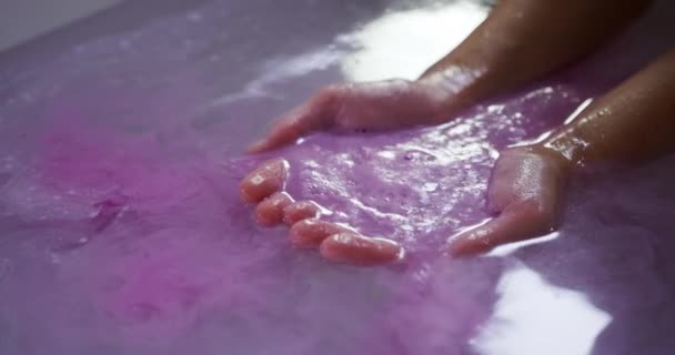 若い白人女性の手を風呂に閉じ 効果的なピンクのバス塩を浴槽の水に入れ ゆっくりとした動き — ストック動画