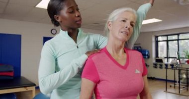 Spor salonundaki muayene koltuğunda oturan, Afrikalı Amerikalı bir kadın fizyoterapistle konuşan, egzersiz programında ona rehberlik eden, boynunu esnetmesine yardım eden,