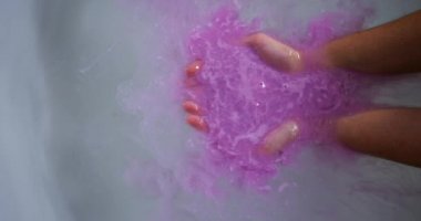 Küvette, küvette, banyo suyunda pembe banyo tuzu tutan, yavaş çekimde, genç, beyaz bir kadının ellerini sıkıca kavra.