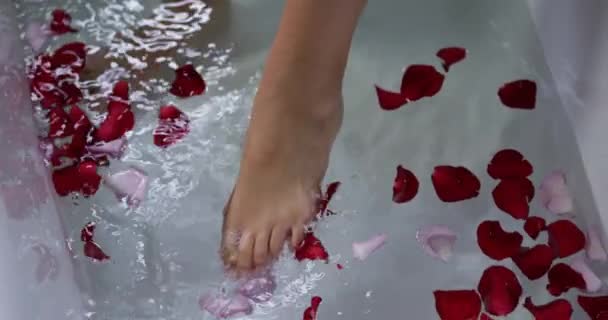 在一个现代化的浴室里 一个年轻的白人女人的脚的下部 走进一个浴池 红色的玫瑰花瓣在水里飘扬 动作缓慢 — 图库视频影像