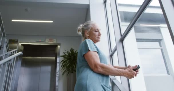 一个白种人女病人假腿站在医院楼梯上用智能手机的侧视图 — 图库视频影像