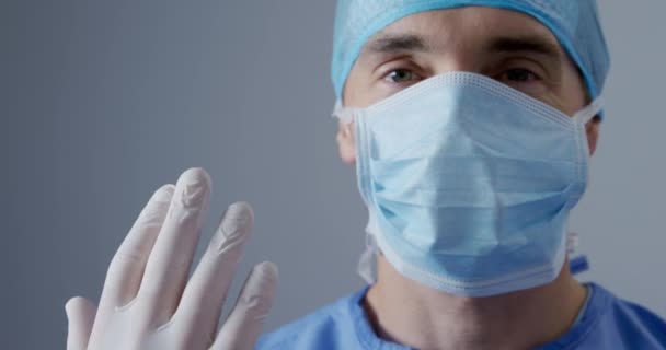 在医院手术室工作的一名白种人男医生头戴刷子 头戴外科帽 戴着口罩 手戴外科手套 望着相机 近视眼前的景象 — 图库视频影像
