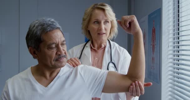 研究室のコートを身に着けている白人女性医師は彼の腕を保持し 観察し 話して 彼の腕の後ろに立つ — ストック動画