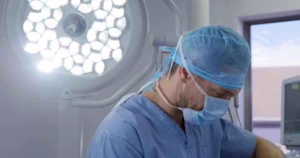 在医院手术室工作的一位身穿洗涤剂 头戴外科帽 戴着口罩 以医疗设备为背景的男性医护人员的侧视特写 — 图库视频影像
