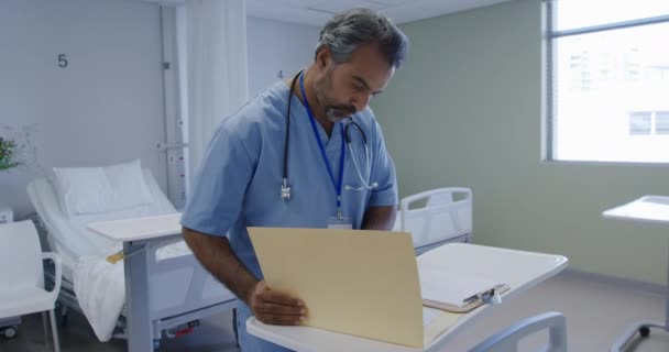 在医院病房里 一名身穿刷子 身份证和听诊器 填写一些文件和走出去的混血男性医疗保健专业人员的照片 — 图库视频影像