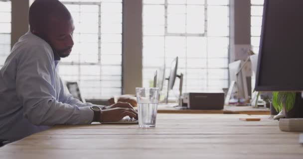 在一个现代化的办公室里 一个年轻的混合种族 富有创造力的职业男子 在办公桌前工作 用笔记本电脑在电话上交谈 动作缓慢 — 图库视频影像