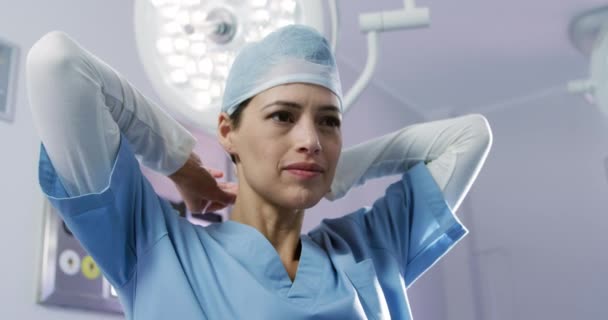 フロントビュー病院の手術室で混合レースの女性医療専門家のクローズアップ スクラブを身に着けていると外科キャップを置く スローモーション — ストック動画