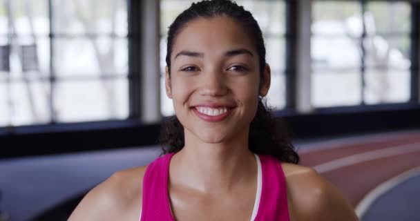スポーツセンターでのトレーニングからの休憩中にカメラに笑顔で スポーツ服を着て運動若い混合人種の白人女性の肖像画 — ストック動画