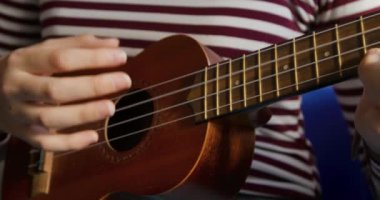 Genç bir müzisyenin orta kesiminde beyaz bir kız çizgili tişört giyiyor ve pratik yapmak için sınıfta ukulele çalıyor.