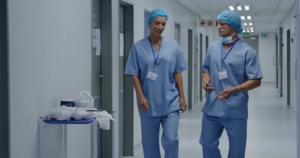 廊下を歩きながら同僚と話す病院の白人アジア系女性医療従事者の正面図 — ストック動画