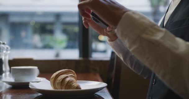 カフェで若い白人のエレガントなビジネスマンの側面図は 彼のスマートフォンでクロワッサンの写真を撮る スローモーション — ストック動画