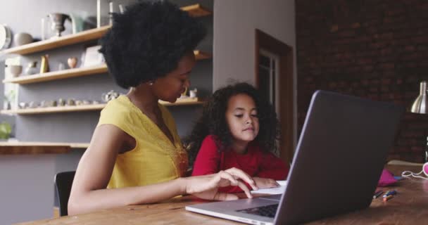 ノートパソコンを見ている母親と一緒にテーブルに座っている若いアフリカ系アメリカ人の女の子の横で — ストック動画