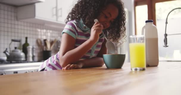 彼女のスプーンと笑顔 彼女の目の前のテーブルの上にオレンジジュースのガラスとそれを混合し 朝食のシリアルのボウルとテーブルに座って ゆっくりと動き — ストック動画
