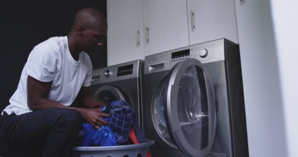 洗濯機 スローモーションに洗濯バスケットから洗濯を入れて 自宅でアフリカ系アメリカ人の男の側面図 — ストック動画