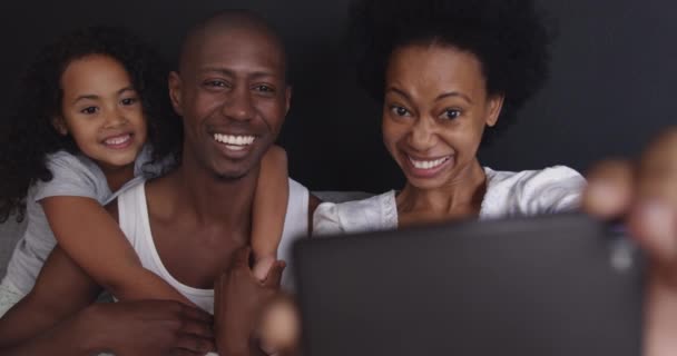 这对非洲裔美国夫妇和他们的年轻女儿一起在客厅里放松 坐在沙发上 抱着她的女儿和她的爸爸 妈妈用智能手机 自拍着他们在一起笑 — 图库视频影像