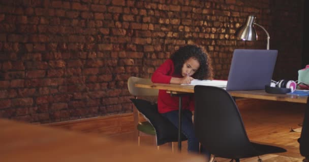 一个年轻的非洲裔美国女孩在家里 坐在餐桌旁 用蜡笔画着 做着功课 面前桌子上有一台笔记本电脑和一盏灯 背景上露出砖墙 动作缓慢 — 图库视频影像